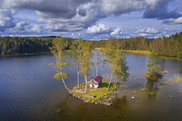 Aerial view over small traditional red wooden cabin on tiny island in lake in autumn, fall,
