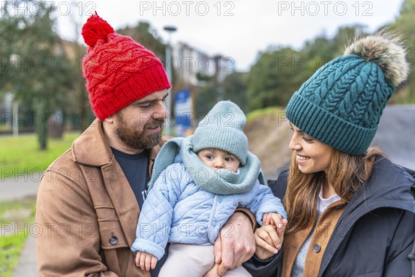 Parents holding their baby while enjoying a leisurely stroll in a park during wintertime, creating