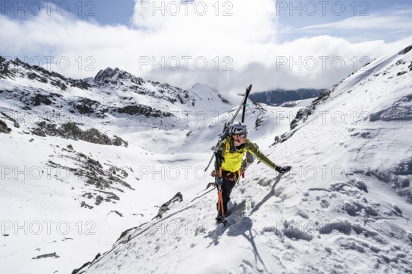 Mountaineer with skis climbing up a steep snow slope to the fork Porta d'Es-cha, ski tour Bündner