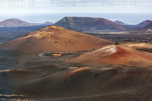 Orange-coloured coach with tourists drives through the fire mountains of Timanfaya National Park,