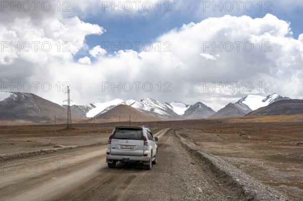 Off-road vehicle on a gravel track, glaciated and snow-covered peaks, Ak Shyrak Mountains, near