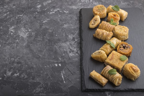 Traditional arabic sweets (kunafa, baklava) on a black slate board on a black concrete background.