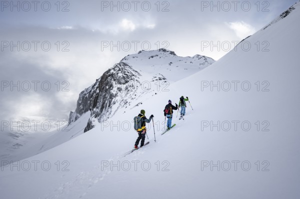Three ski tourers in a snowy mountain landscape in the morning light, ascent to the Wildhorn,