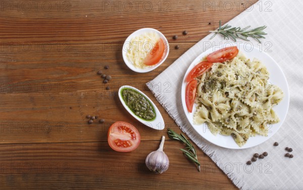 Farfalle pasta with pesto sauce, tomatoes and cheese on a linen tablecloth on brown wooden