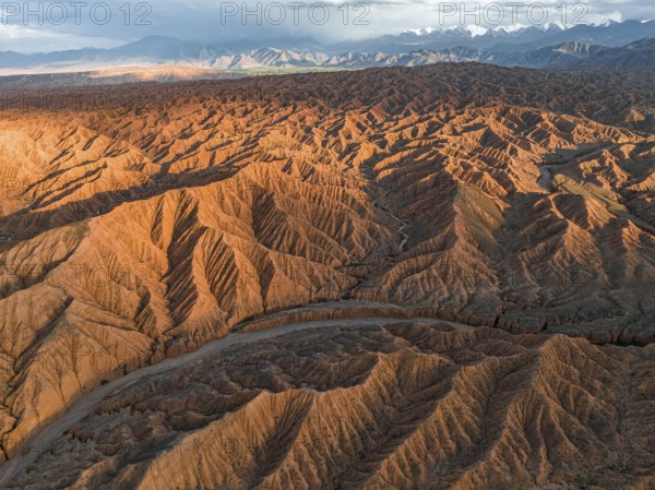 River bed runs through a landscape of eroded hills, badlands at sunset, mountain peaks of the Tian
