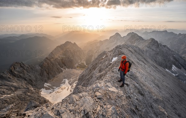 Mountaineer with helmet on a narrow rocky ridge at sunrise, crossing the Jubiläumsgrat, view of