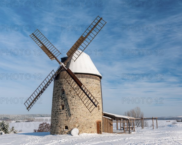 The tower windmill of Warnstedt in winter surrounded by snow-covered landscape under a blue sky,