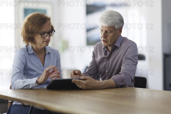 Symbolic photo. A woman and a man sit together at a table with a tablet and talk. Berlin, 13.08