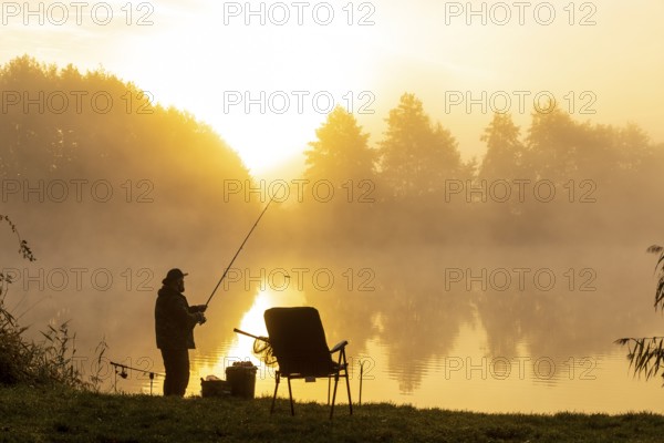 Angler on the bank at sunrise in the fog at the Grutschenteich in Nassau, Weinböhla, Saxony,