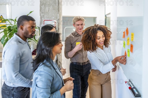 Diverse team collaborating, using sticky notes on a whiteboard during a brainstorming session in a