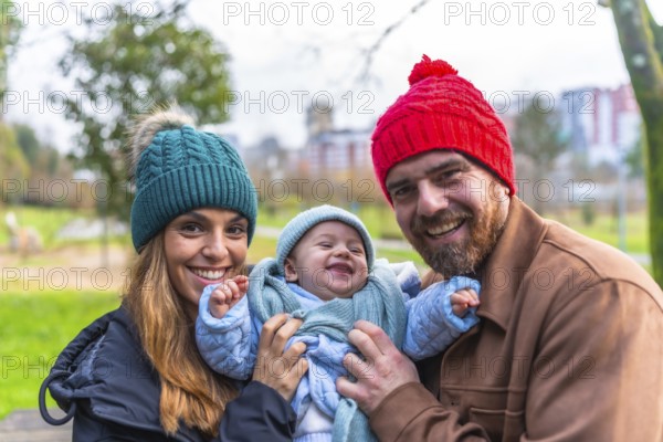 Smiling parents holding their laughing baby wearing winter clothes, enjoying a sunny winter day at