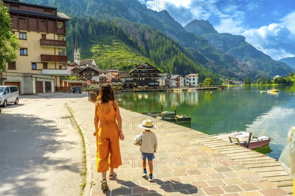 Mother and son walking on a paved pathway by the alleghe lake in the italian dolomites, enjoying