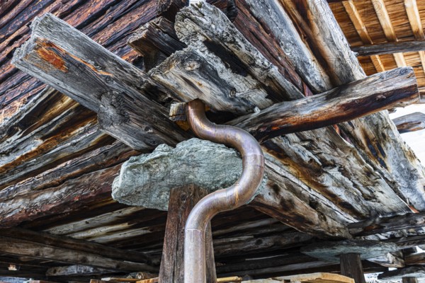 Old weathered hay barn with wooden support, stone slab and copper pipe, Chandolin, Val d'Anniviers,