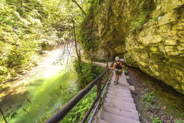 Tourists wearing helmets are walking down wooden stairs along the radovna river in vintgar gorge, a