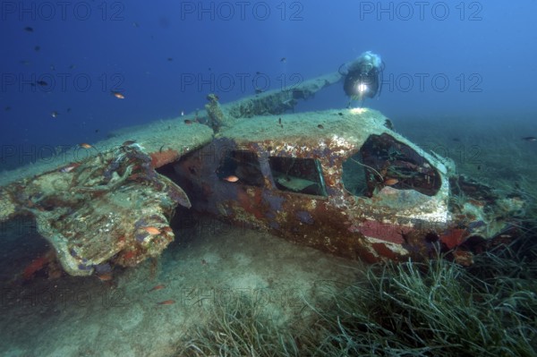Diver looking at Cessna aircraft wreck underwater on the seabed while scuba diving, Porto Azzurro,