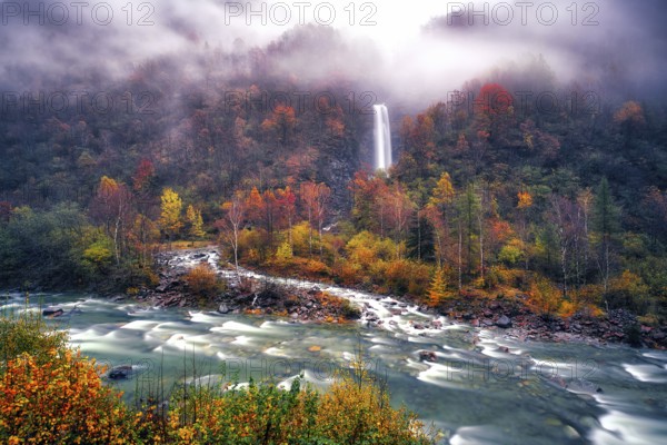 Waterfall with river Verzasca surrounded by autumn coloured deciduous trees, rainy and foggy