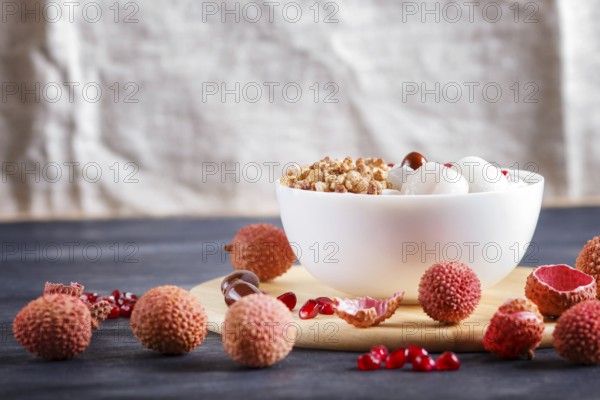Greek yogurt with lychee, pomegranate seeds and granola in a white plate on a black wooden