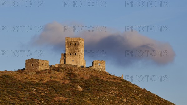 Sunset colours the clouds over the imposing ruins of a fortress on a mountain, residential tower on