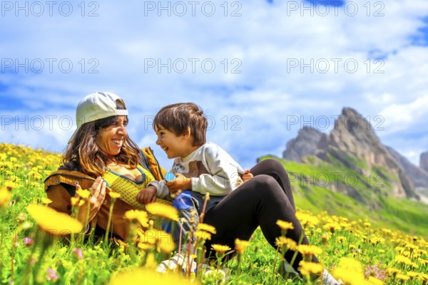 Mother and son relaxing in a dandelion field, enjoying the breathtaking view of the seceda