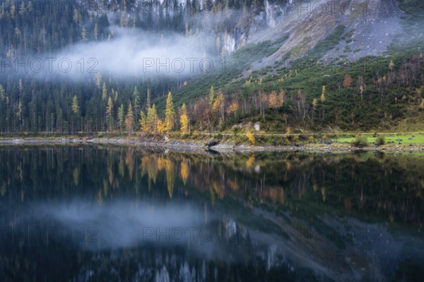 The Vordere Gosausee in autumn. Part of the path around the lake, with a cloud. Trees in autumn