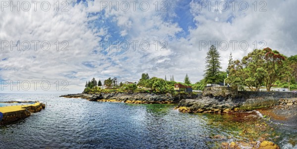 Coastal landscape with houses and trees under a serene sky, the calm sea surrounds the rocky coast,