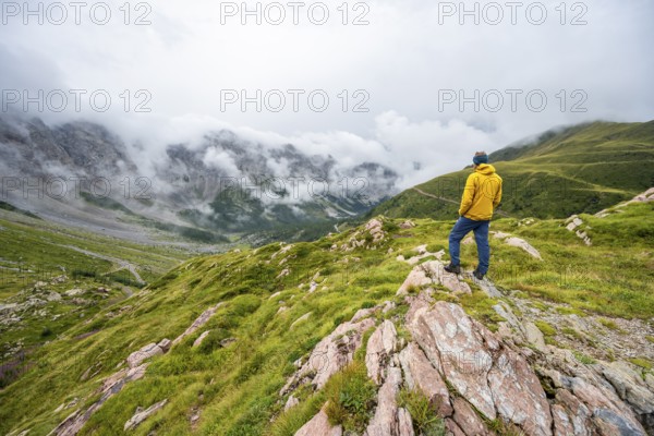 Mountaineer with yellow jacket looking at mountain landscape, cloudy rocky mountain peaks Wolayer