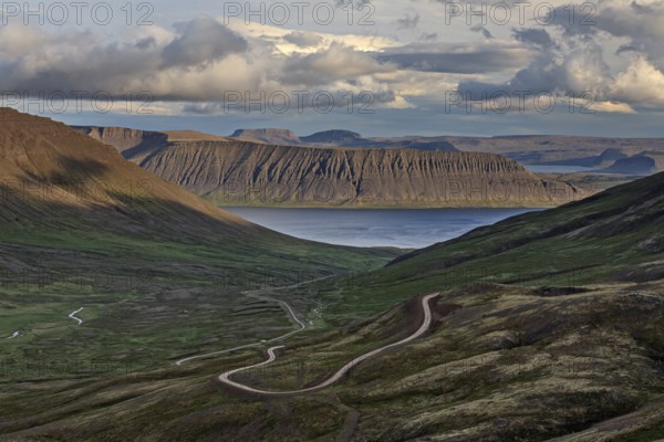 Winding gravel road, mountain road, fjord and mountains behind, cloudy mood, summer, Westfjords,
