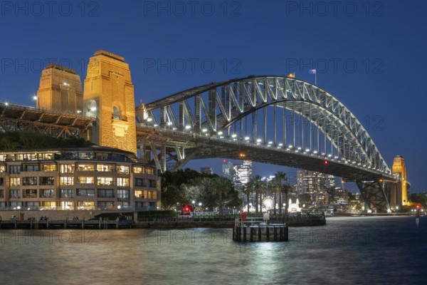 Sydney Harbour Bridge at night, illuminated at blue hour, with city lights in the background and
