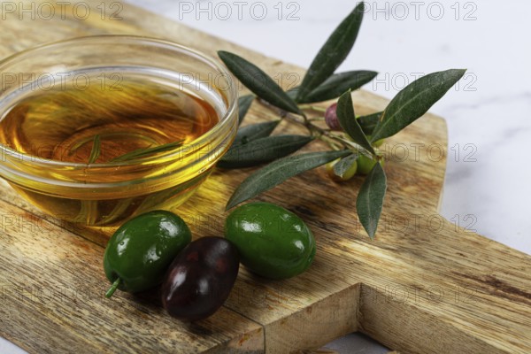 A glass bowl filled with rich olive oil sits on a wooden cutting board alongside fresh green and