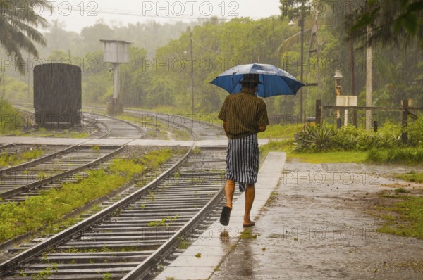 Sinhalese with umbrella in heavy rain, monsoon, railway station in Kalawewa, Sri Lanka, Ceylon,