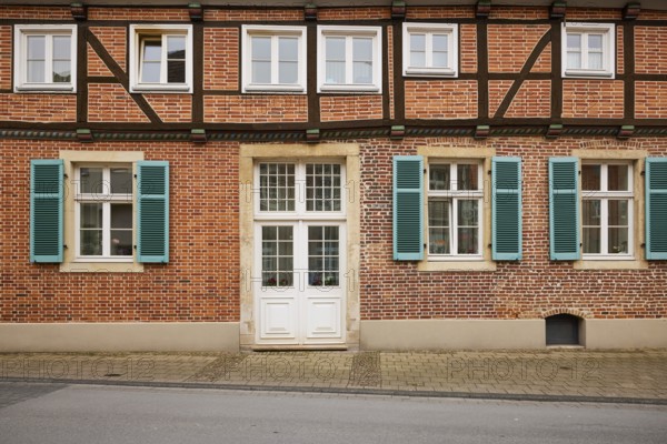 Facade of a half-timbered brick house with white windows, a mighty entrance door and blue-green