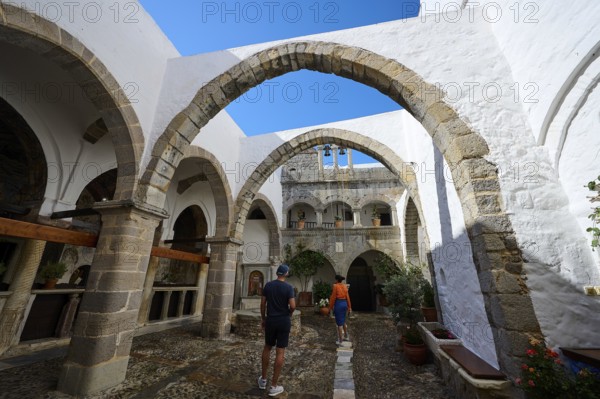 Historic monastery courtyard with stone arcades and bright white walls. Tourists explore the