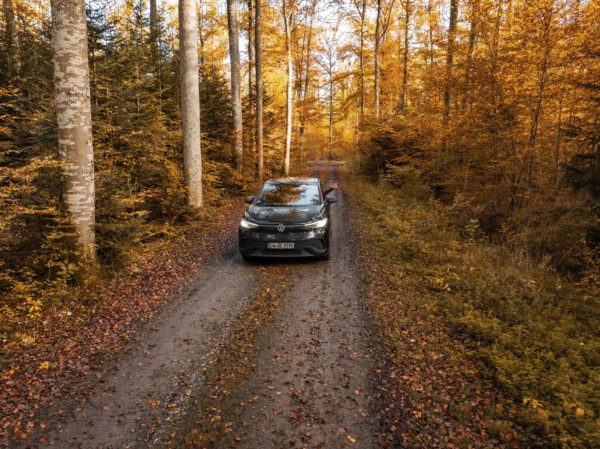 Car standing on a forest path, surrounded by autumn trees and leaves, electric car, VW ID5,