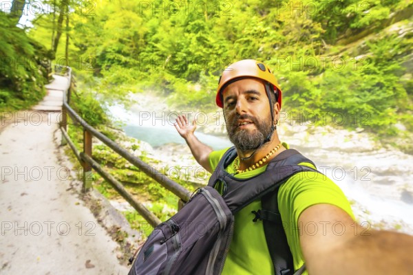 Tourist wearing an orange helmet and backpack takes a selfie while visiting vintgar gorge near bled