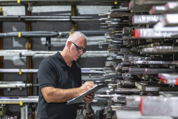 Side view photo of a mature caucasian man checking metal bars while doing inventory using a