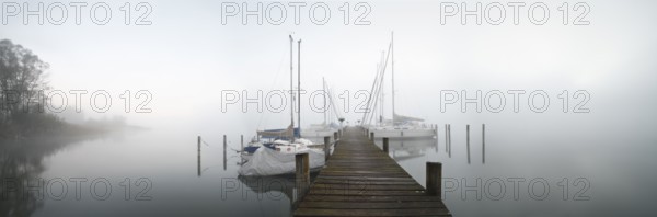 Quiet autumn morning on Lake Chiemsee, jetty with sailing boats in dense fog, Prien am Chiemsee,