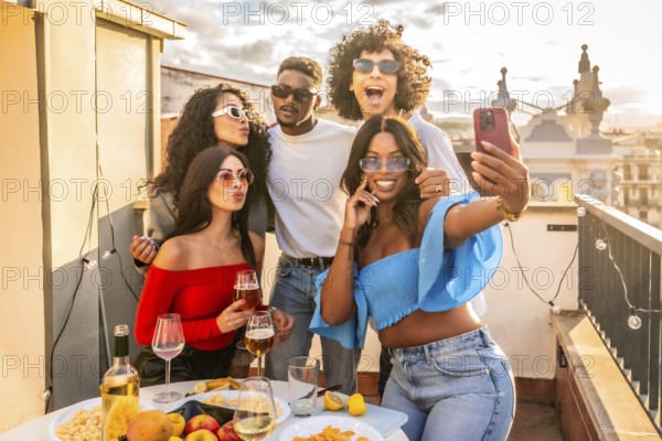 Happy multi-ethnic friends taking selfie celebrating evening party in rooftop drinking wine and