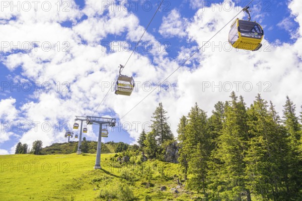 Several cable cars travelling across a green meadow under a cloudy sky, Penken, Zillertal, Austria,