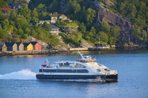 Colourful wooden houses by the water, surrounded by dense forest and hills, a ferry sails on the