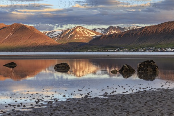 Fjord, low tide, stones, mountains reflected in the water, evening light, cloudy mood, Thingeyri,