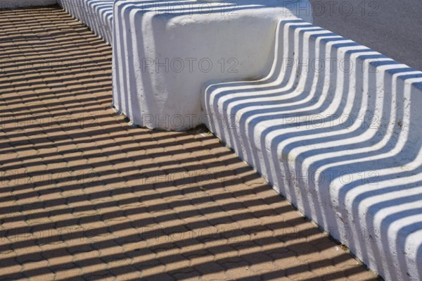 White concrete bench with geometric shadow patterns on a brown floor, Saintes-Maries-de-la-Mer,