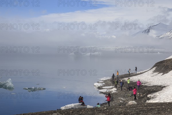 Tourists standing at glacier lagoon, ice floes, glacier, fog, winter, sunny, Jökulsarlon, Iceland,