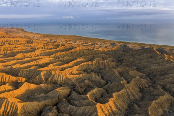 Landscape of eroded hills, badlands at sunset, Lake Issyk Kul in the background, aerial view,