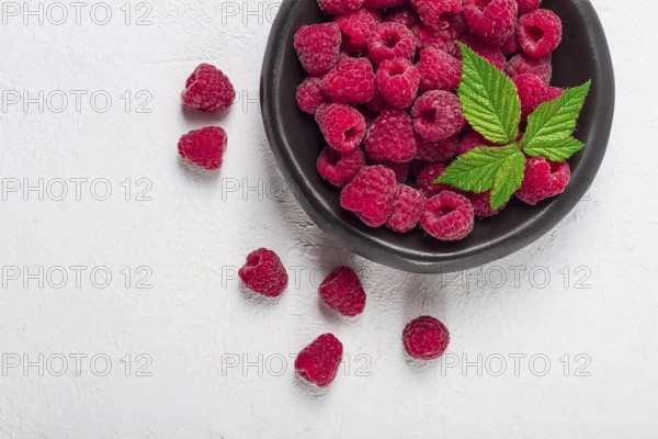 Fresh raspberries, on a black plate, with leaves, top view, on a white table