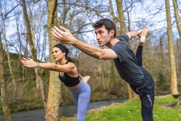 Yoga teachers performing a balancing asana by a river in the forest, enjoying the benefits of