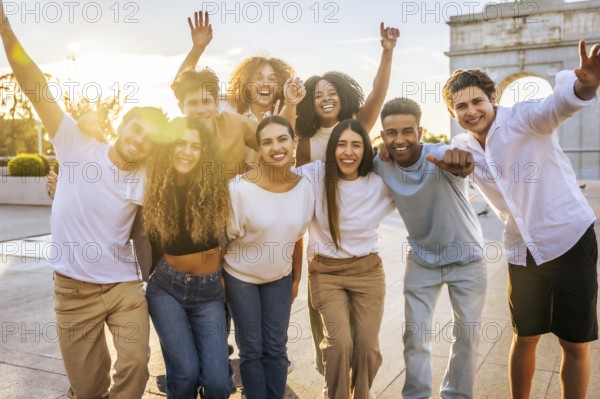Portrait of diverse group of cheerful young people having fun and raising arms while standing