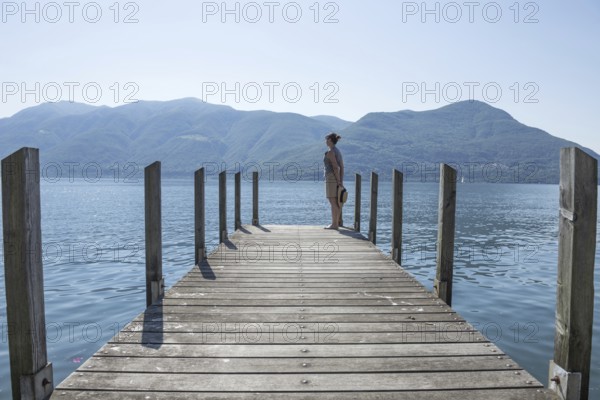 Woman Standing on a Pier on Lake Maggiore with Mountain in a Sunny Day in Brissago, Ticino,