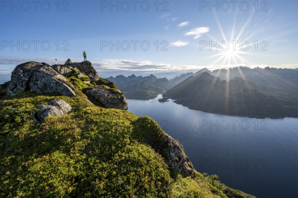Mountaineer on the summit of Dronningsvarden or Stortinden, behind sea and fjord Umvågsundet,