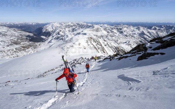 Ski tourer on foot, carrying skis on backpack, mountain panorama, snow-covered mountain landscape