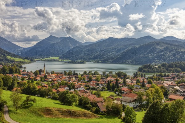 Picturesque lakeside village in the Alps, surrounded by green meadows and mountains under a cloudy